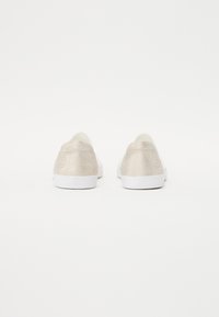 Fémes bézs színű slip-on cipők fehér talppal, sima felülettel és visszafogott logóval a saroknál. Csak hátsó nézet.