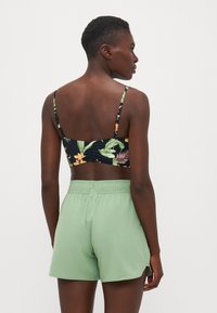Svart blomstrete sportsh_br med tynne stropper, kombinert med lysegrønne shorts med elastisk midje. Glatt tekstur, avslappet design og ingen synlig maskinvare.