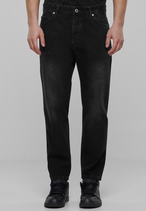Sorte denimbukser med lige ben, fem lomme-design og sølvfarvede hardware detaljer. Båret med sorte sneakers.