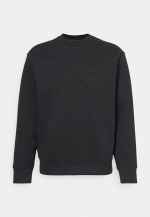 Sweatshirt noir avec un col rond côtelé, logo texturé sur la poitrine et manches longues ; fabriqué en tissu doux et tissé.