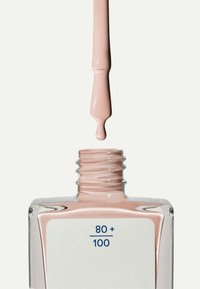 Nagellakfles met een helder glazen ontwerp, gevuld met zachte roze lak; een druppel hangt van de kwast erboven, het etiket leest "80 + 100."