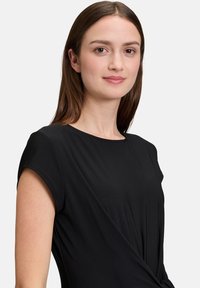 Zwarte korte mouwen top met een ronde halslijn, voorzien van een gedraaide ontwerpdato bij de taille. Stijve textuur en een ontspannen pasvorm.