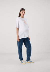 White t-shirt with a graphic print featuring a cartoon character, paired with blue denim jeans and white sneakers with blue stripes.