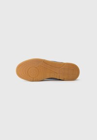 Blå sneakersål med en struktureret gummioverflade og en gummigummisål, udstyret med riller for greb og et rundt logo.