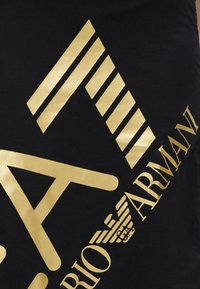 Μαύρο T-shirt με μεγάλο χρυσό λογότυπο, γεωμετρικά σχέδια και κείμενο "EA7" και "Armani" σε κομψό σχέδιο.