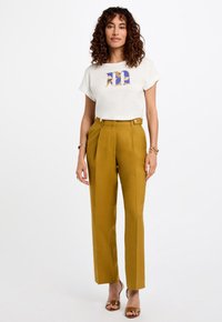 Lichte crème t-shirt met een kleurrafiek, gecombineerd met hoog-geprojecteerde mosterdkleurige broeken met plooien en een ceintuurdetail.