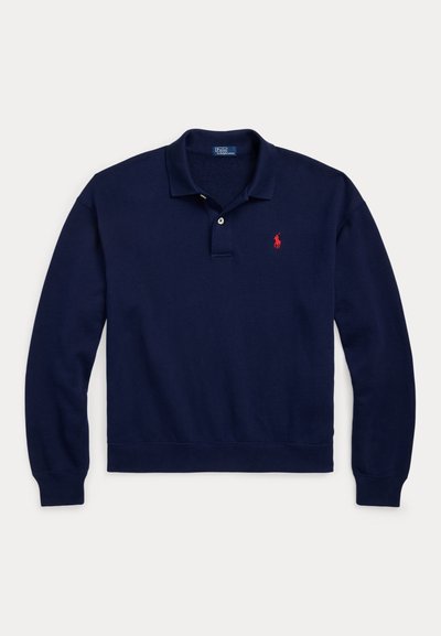 Tumesinine pika varrukaga polosärk kraega, kahe nupuga klapiga, soonikkoes mansettide ja äärega ning väike punane tikitud logo rinnal.