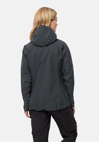 Waterdichte donkergrauwe jas met een capuchon, met een gladde textuur, een getailleerd ontwerp en subtiele naden, gedragen met zwarte broek.