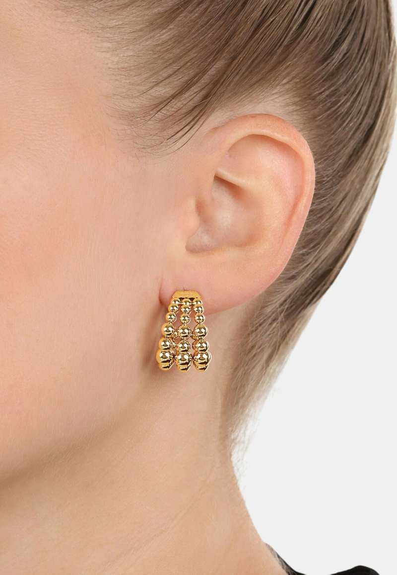 Pendientes de metal en tono dorado que presentan tres filas de cuentas esféricas, creando un diseño de caída en cascada. La superficie es brillante y reflectante.