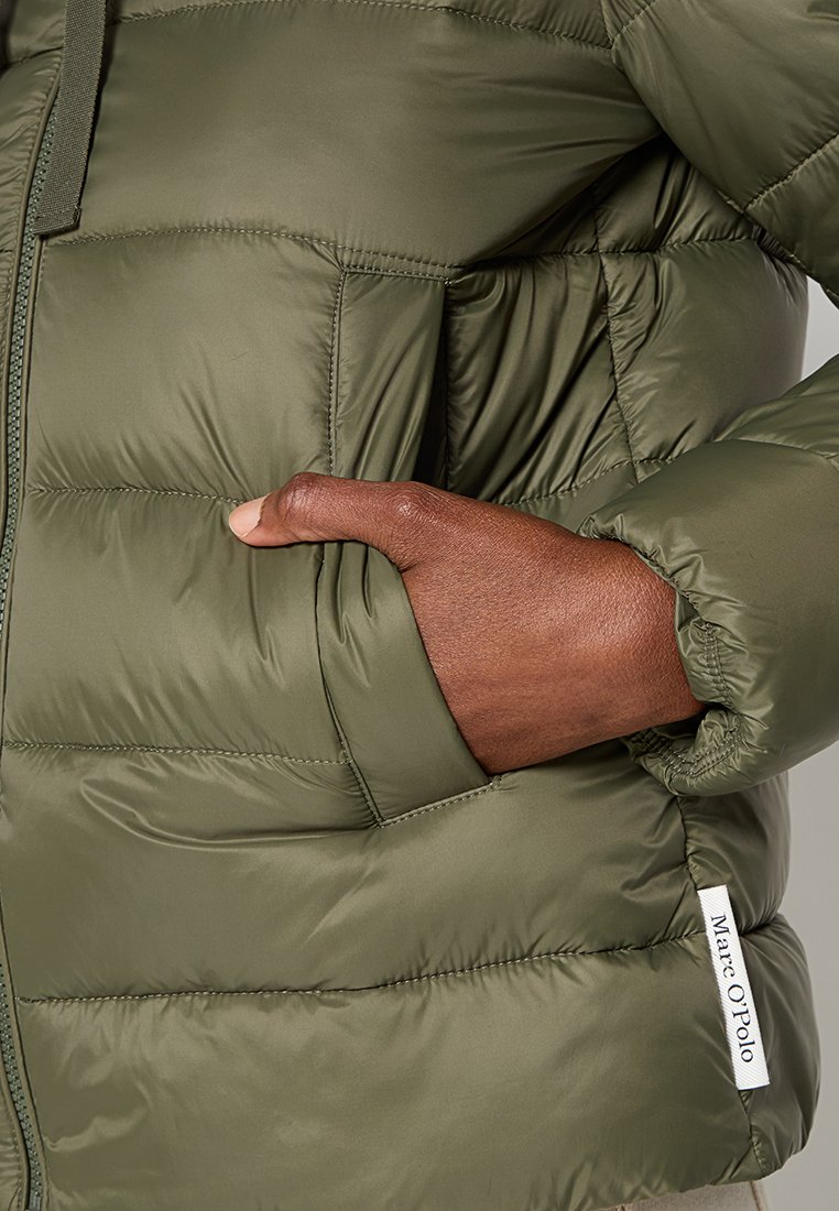 Olívazöld, steppelt pufi dzseki, az oldalsó varráson a Marc O'Polo márka logójával, zsebben lévő kéz.