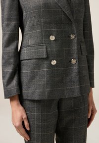 Blazer grigio a quadri con bottoni doppi, rever a spine e tessuto testurizzato. Include tasche laterali e vestibilità sartoriale.