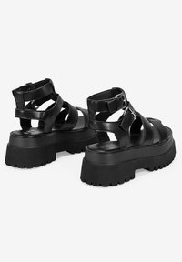 Sandalias de plataforma negras con diseño de múltiples correas, fabricadas en cuero suave. Suela de goma gruesa con agarre texturizado y correas ajustables en el tobillo.