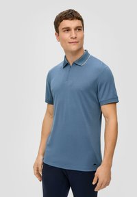 Koszulka polo w miękkim niebieskim materiale, z żebrowanym kołnierzykiem i krótkimi rękawami, z białym akcentem wzdłuż krawędzi kołnierza.