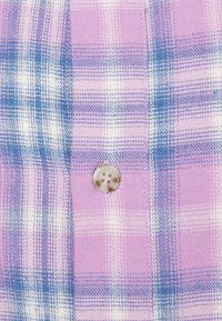 Gros plan sur un tissu à carreaux rose et bleu avec un seul bouton clair à quatre trous cousu au centre.