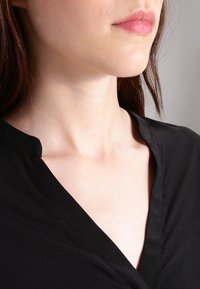 Schwarze V-Ausschnitt-Bluse mit einer weichen Textur, kleinen Kragen und einem glatten, fließenden Stoff, der den Ausschnitt umschmeichelt.