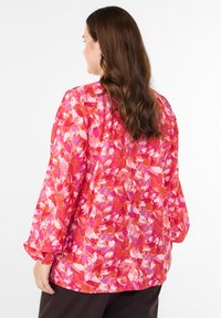 Kolorowa bluzka w kwiatowy wzór w odcieniach różu i czerwieni. Długie rękawy z elastycznymi mankietami, lekka tkanina i luźny krój.