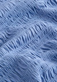 Tissu bleu clair avec des lignes verticales texturées, froncées et plissées créant une apparence douce et froissée.