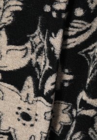 Tejido de lana con un patrón floral en negro y beige. Textura suave con un acabado ligeramente difuso, formas oscuras sobre un fondo claro.