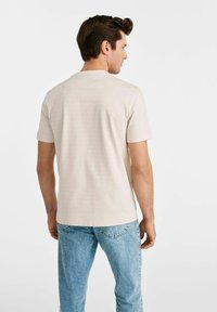 Beżowy t-shirt z krótkim rękawem i okrągłym dekoltem, wykonany z miękkiej tkaniny, połączony z jasnoniebieskimi dżinsami. Prosty, minimalistyczny design.