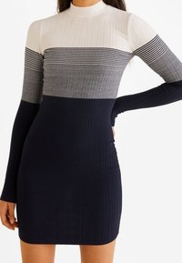 Femme portant une robe à manches longues côtelée avec des sections horizontales colorblock en blanc, rayé noir, gris et bleu marine.