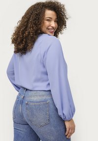 Helle lila Bluse mit langen Puffärmeln, kombiniert mit hochgeschnittenen blauen Jeans. Glattes Material, lockere Passform und schlichtes Design.
