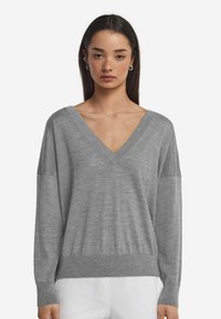 Grauer V-Ausschnitt-Pullover mit langen Ärmeln, lockerer Passform und geripptem Saum. Weiches, leichtes Material mit feiner Textur.