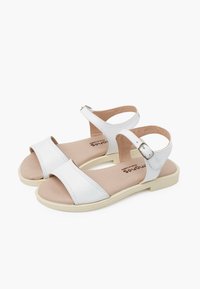 White women's sandals with two wide straps, adjustable ankle buckle, soft beige insole, and lightweight sole, featuring minimalistic design.