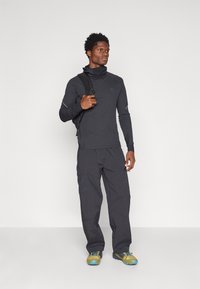 Cămașă neagră pentru bărbați cu mâneci lungi și guler înalt, asortată cu pantaloni cargo închisi la culoare. Încălțămintea include adidași gri cu galben.