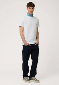 Witte t-shirt met korte mouwen en een blauwe patroonkraag, gecombineerd met donkerblauwe jeans en beige sneakers met lichtblauwe veters.
