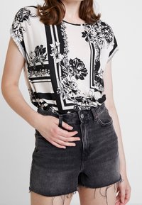Svart och vit mönstrad blus med korta ärmar, tillsammans med högmidjade svarta denim-shorts. Blusen har blommiga och geometriska mönster.