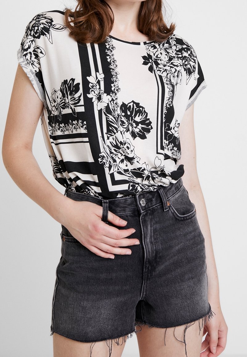 Svart och vit mönstrad blus med korta ärmar, tillsammans med högmidjade svarta denim-shorts. Blusen har blommiga och geometriska mönster.