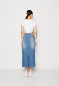 Vit kortärmad t-shirt och lång jeanskjol med en ljus till mörkblå gradient, två bakfickor och en sidoremsdetalj. Ljust rosa klackar.