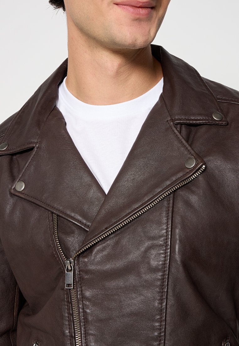 Man in een donkerbruin leren jack met rits, drukknopen en een wit T-shirt eronder.