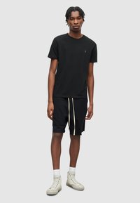 Černé bavlněné tričko s kulatým výstřihem, v kombinaci s černými kraťasy s bílou šňůrkou. Oblečeno s světlými teniskami.