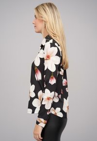 Zwarte bloes met grote witte en roze bloemen, lange mouwen en een ontspannen pasvorm, gemaakt van een zachte stof.