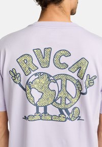 Camiseta de algodón de color púrpura claro con un diseño gráfico que presenta un globo terráqueo y un símbolo de paz, contorneado en azul oscuro con acentos amarillos punteados.