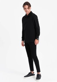 Musta pitkähihainen poolopaita, valmistettu puuvillasta, yhdistettynä mustiin kapeisiin housuihin ja mustiin lenkkareihin, joissa on valkoinen pohja. Yksinkertainen muotoilu, ei kuvioita.