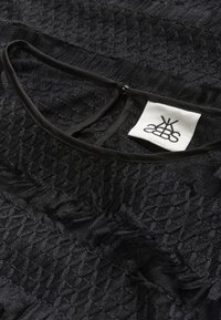 Tissu noir texturé avec un motif tissé. Présente un col rond avec un bord noir et une petite étiquette affichant un logo.