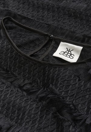 Crna teksturirana tkanina s tkanim uzorkom. Ima okrugli izrez s crnim obrubom i malu oznaku s prikazom loga.