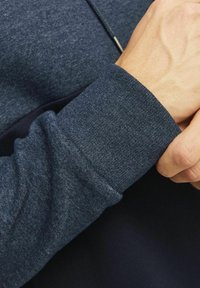 Sudadera azul marino con una tela texturizada. Primer plano de la manga, que presenta un acabado acanalado y un ajuste ceñido alrededor de la muñeca.