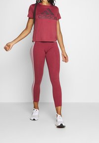Maroon Adidas lyhyt toppi mustalla logolla; matching maroon legginsit valkoisilla sivuraidoilla ja tiukalla designilla; valkoiset urheilukengät.
