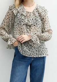 Blouse fleurie et transparente avec volants au niveau du col et des poignets, comprenant un détail à lacets. Fond noir avec motif floral blanc. Coupe élégante et texturée.