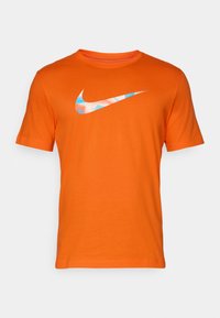 Oranje katoenen t-shirt met korte mouwen, met daarop een blauw-wit Nike-logo over de borst. Ronde halslijn, klassieke pasvorm.