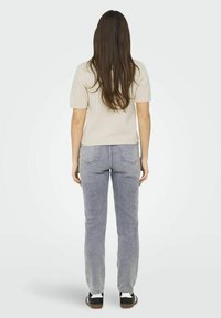 Beige gebreide top met korte mouwen, aansluitend in de taille, gecombineerd met lichtgrijze rechtvallende spijkerbroek en zwarte sneakers met witte accenten.