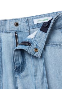 Pantalones de mezclilla azul claro con un corte amplio, con cierre de botón, cremallera y detalles en azul oscuro. La etiqueta dice "AVRIL-WIDE."