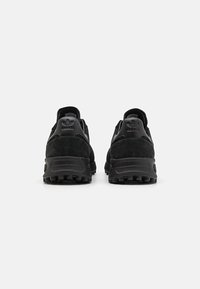 Zwarte suède sportschoenen hebben een gestructureerde bovenkant, een gevoerde kraag en een rubberen buitenzool met gripnoppen. Logo gedrukt op de hiel.