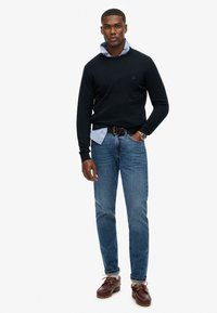 Marineblå trøje over en lys blå skjorte med krave, parret med blå jeans og brune snørebåndssko. Enkel design og klassiske farver.
