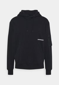 Svart hoodie i mjukt tyg, med en känguruficka, justerbar dragsko i huvan, samt en ficka med patch på vänster ärm.