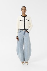 Hvit strikket cardigan med svarte detaljer og knapper, kombinert med oversized lyseblå denimjeans og hvite spisse hæler.