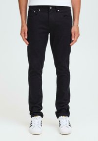 Svarte bomullsjeans med slim fit, fem lommer og metallknapper. Båret med hvite sneakers som har svarte striper.